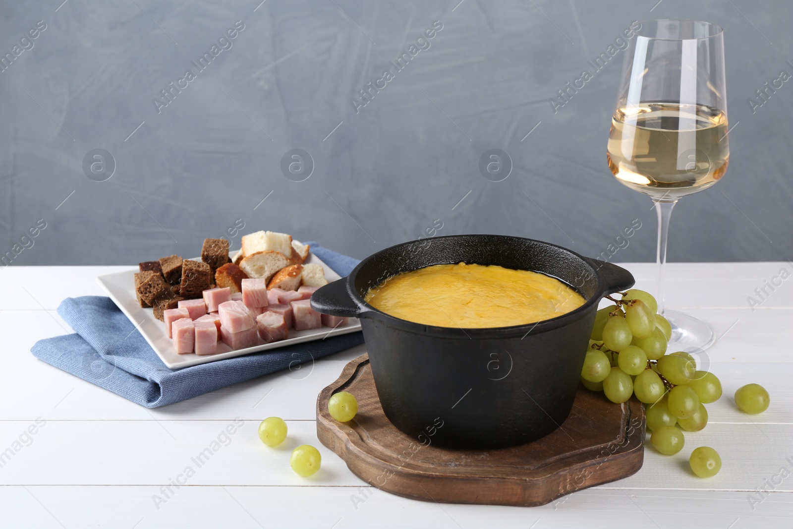 Photo of Fondue with tasty melted cheese, different products and aromatic wine in glass on white wooden table