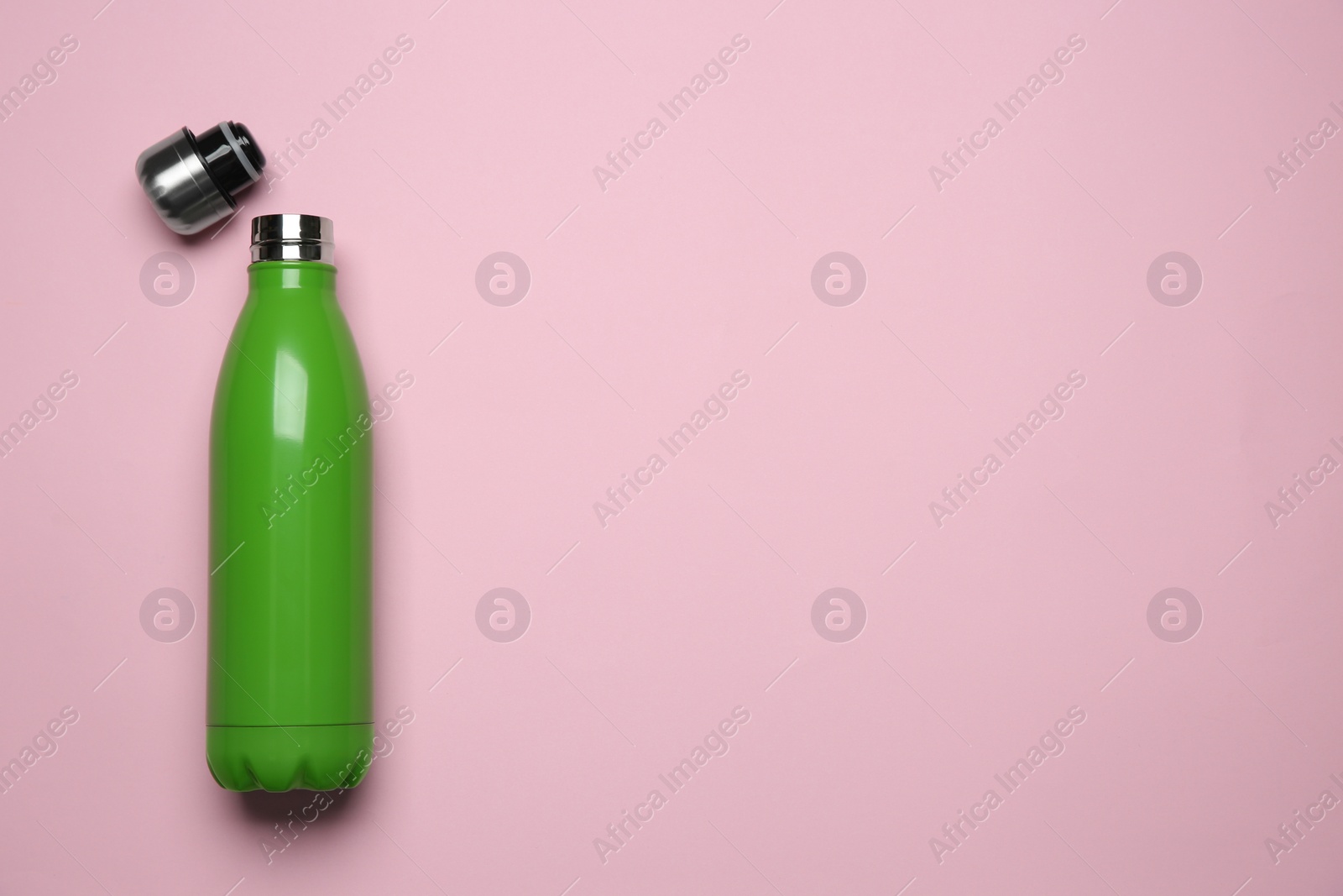 Photo of Green thermo bottle on pink background, top view. Space for text