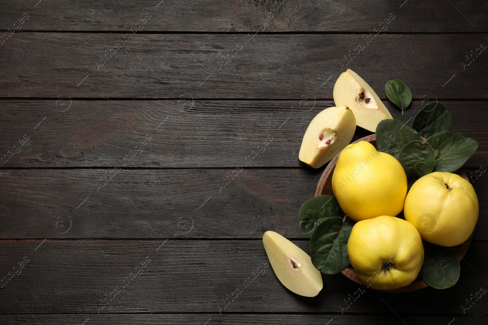 Photo of Fresh ripe organic quinces with leaves on wooden table, flat lay. Space for text