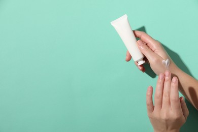 Woman with tube applying cosmetic cream onto her hand on turquoise background, top view. Space for text