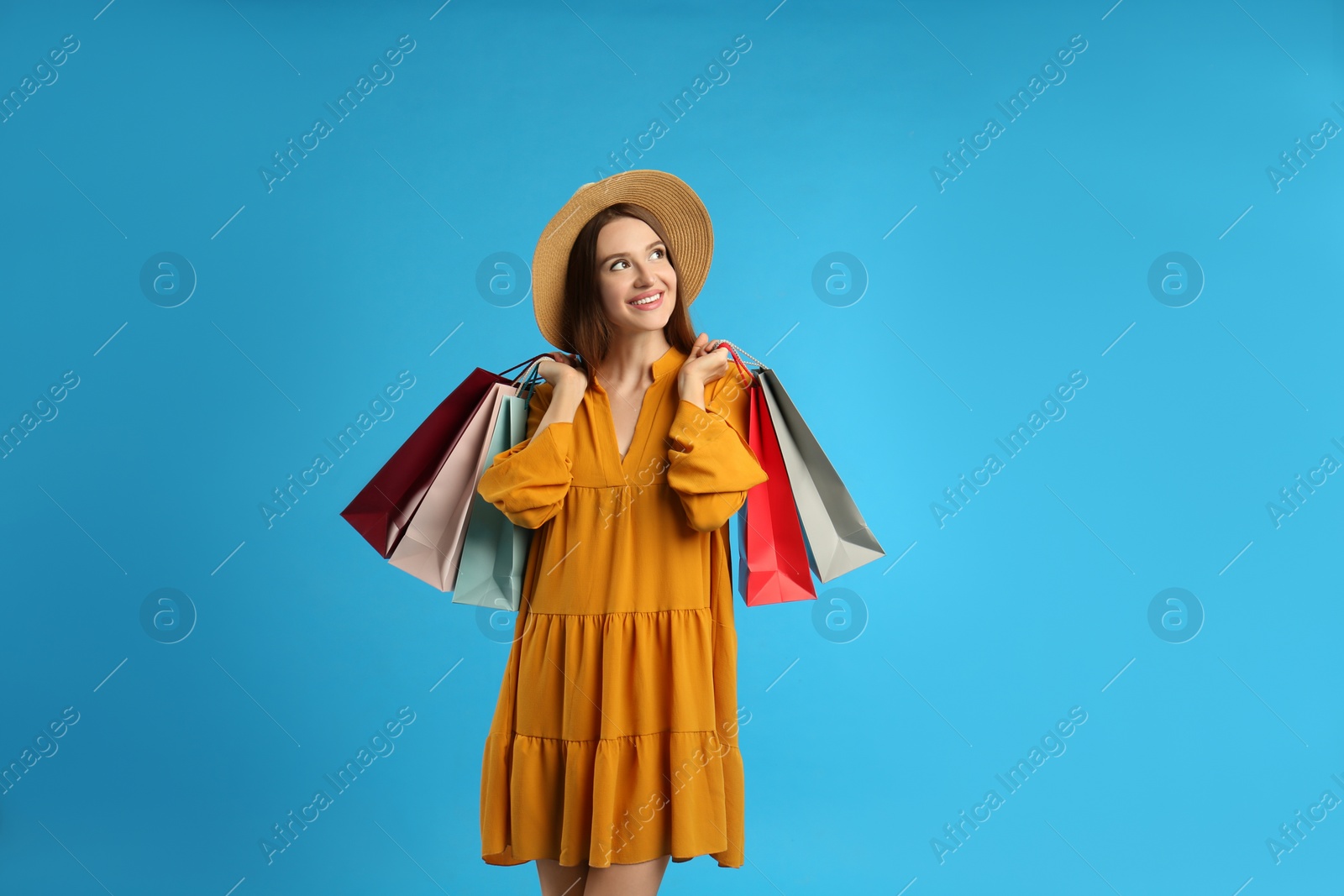 Photo of Beautiful young woman with paper shopping bags on light blue background