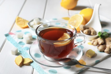 Cup of delicious ginger tea, sugar cubes and lemons on white wooden table