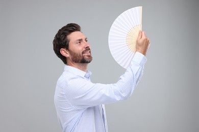 Happy man holding hand fan on light grey background