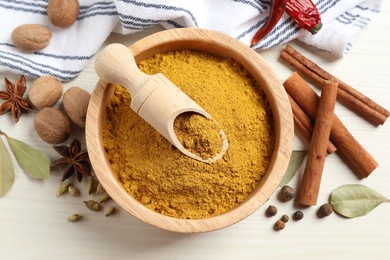 Dry curry powder in bowl and other spices on light wooden table, flat lay