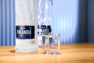 MYKOLAIV, UKRAINE - SEPTEMBER 23, 2019: Finlandia vodka and shot glasses on wooden bar counter. Space for text