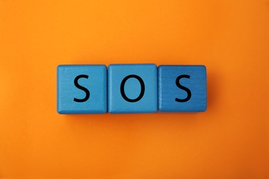 Photo of Abbreviation SOS (Save Our Souls) made of blue cubes with letters on orange background, top view