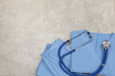Photo of Medical uniform and stethoscope on light grey table, top view. Space for text