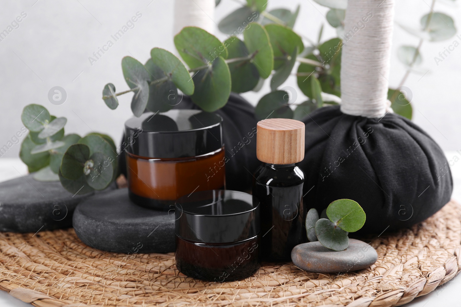 Photo of Spa composition with cosmetic products, herbal massage bags, stones and eucalyptus branches on table