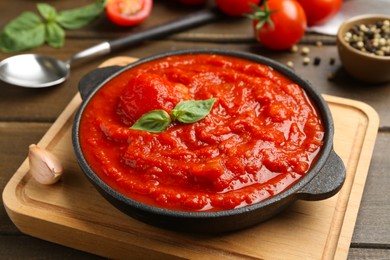 Photo of Homemade tomato sauce and basil in bowl on wooden table, closeup