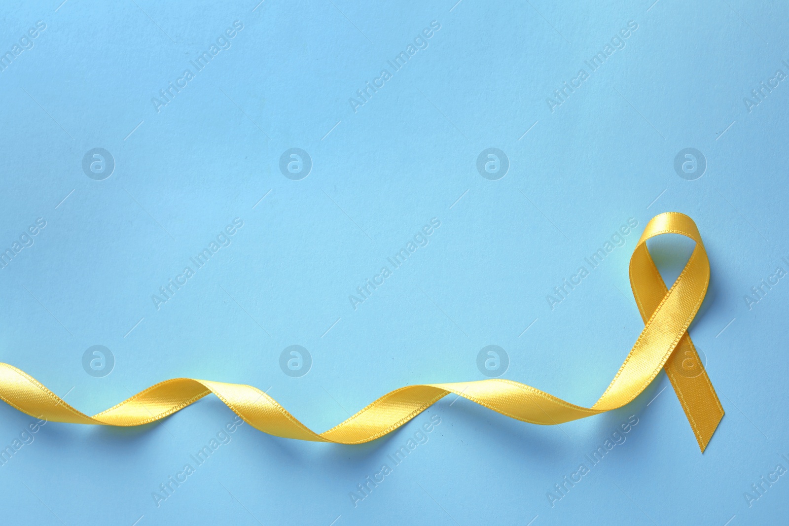 Photo of Yellow ribbon on color background, top view. Cancer awareness