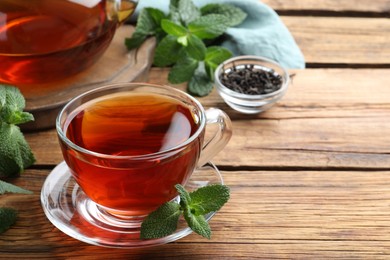 Photo of Cup of aromatic black tea with fresh mint on wooden table. Space for text