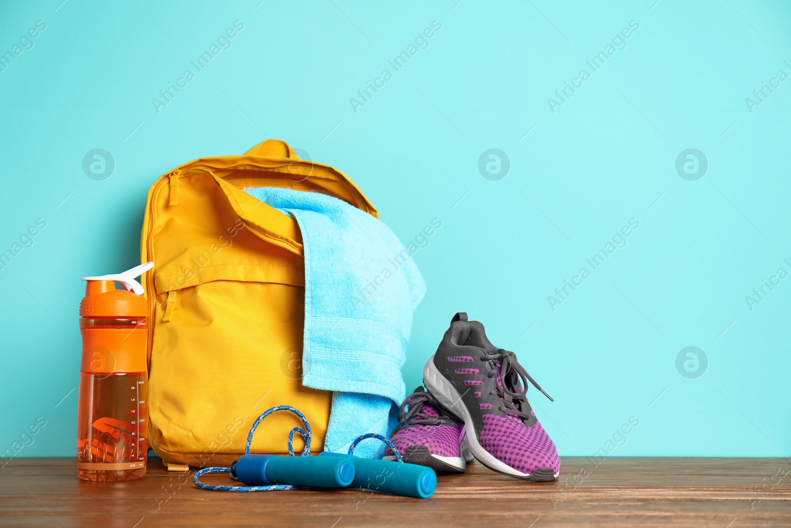 Photo of Sports bag and gym equipment on wooden floor against color background