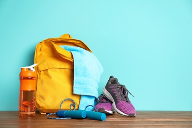 Photo of Sports bag and gym equipment on wooden floor against color background