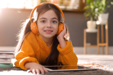 Cute little girl with headphones wearing orange knitted sweater at home