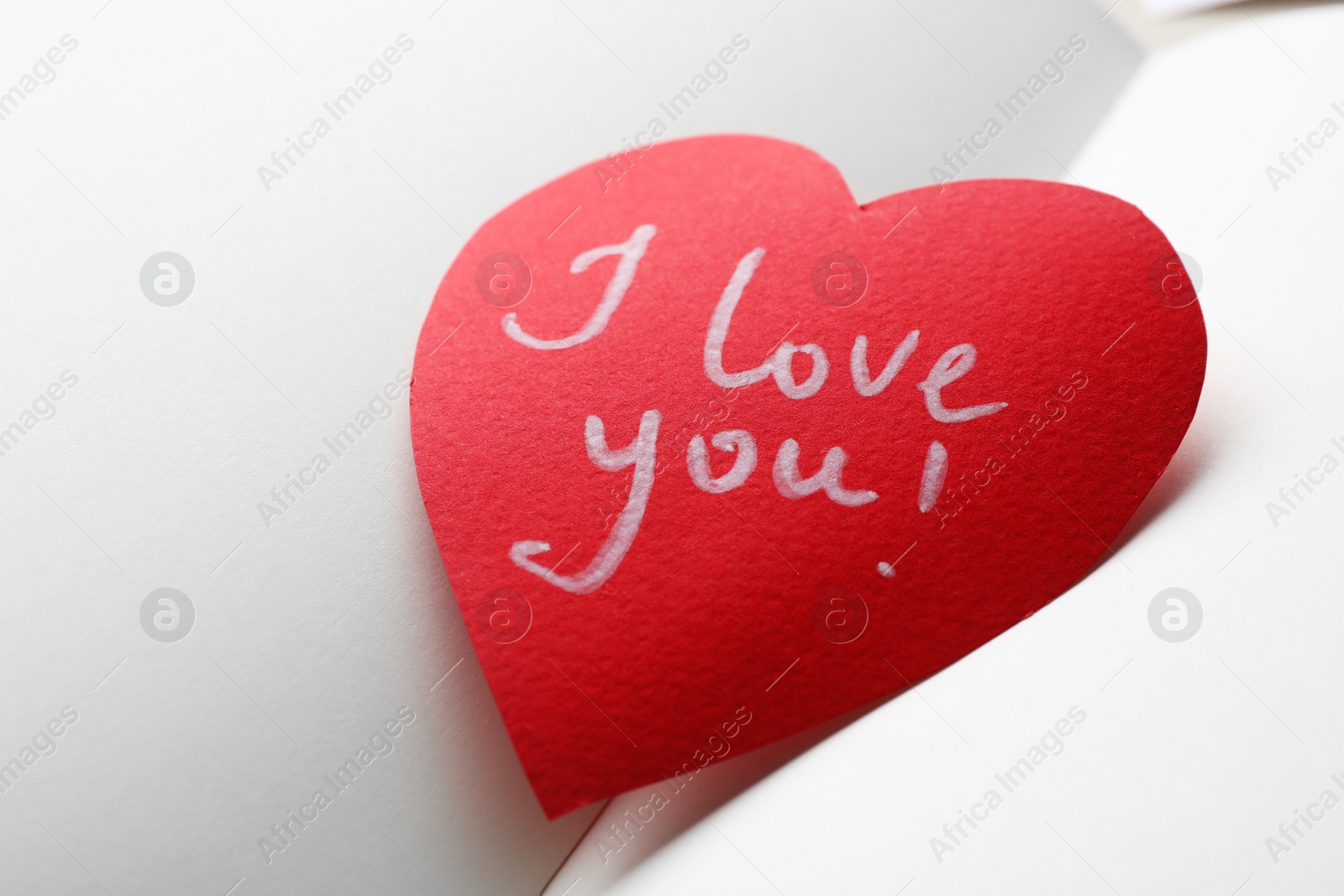 Photo of Paper heart with words I LOVE YOU on open notebook, closeup