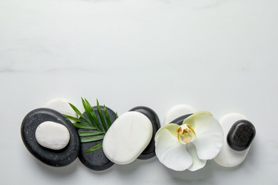 Photo of Flat lay composition with spa stones, orchid flower and leaf on white marble table. Space for text