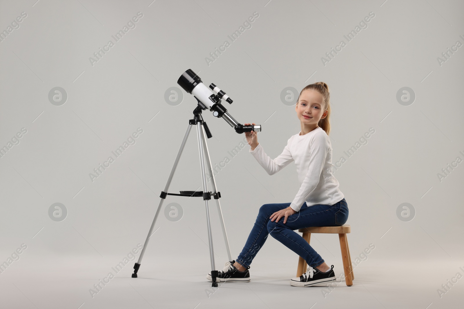 Photo of Happy little girl with telescope on light grey background