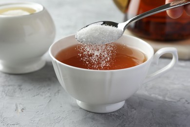 Photo of Adding sugar into cup of tea at grey textured table, closeup