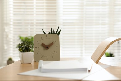 Notebook, clock and houseplants on table indoors