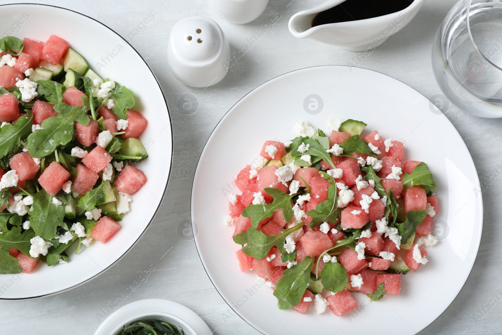 Photo of Delicious salad with watermelon, cucumber, arugula and feta cheese served on white wooden table, flat lay