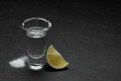 Photo of Mexican Tequila shot with salt and lime slice on black table. Space for text