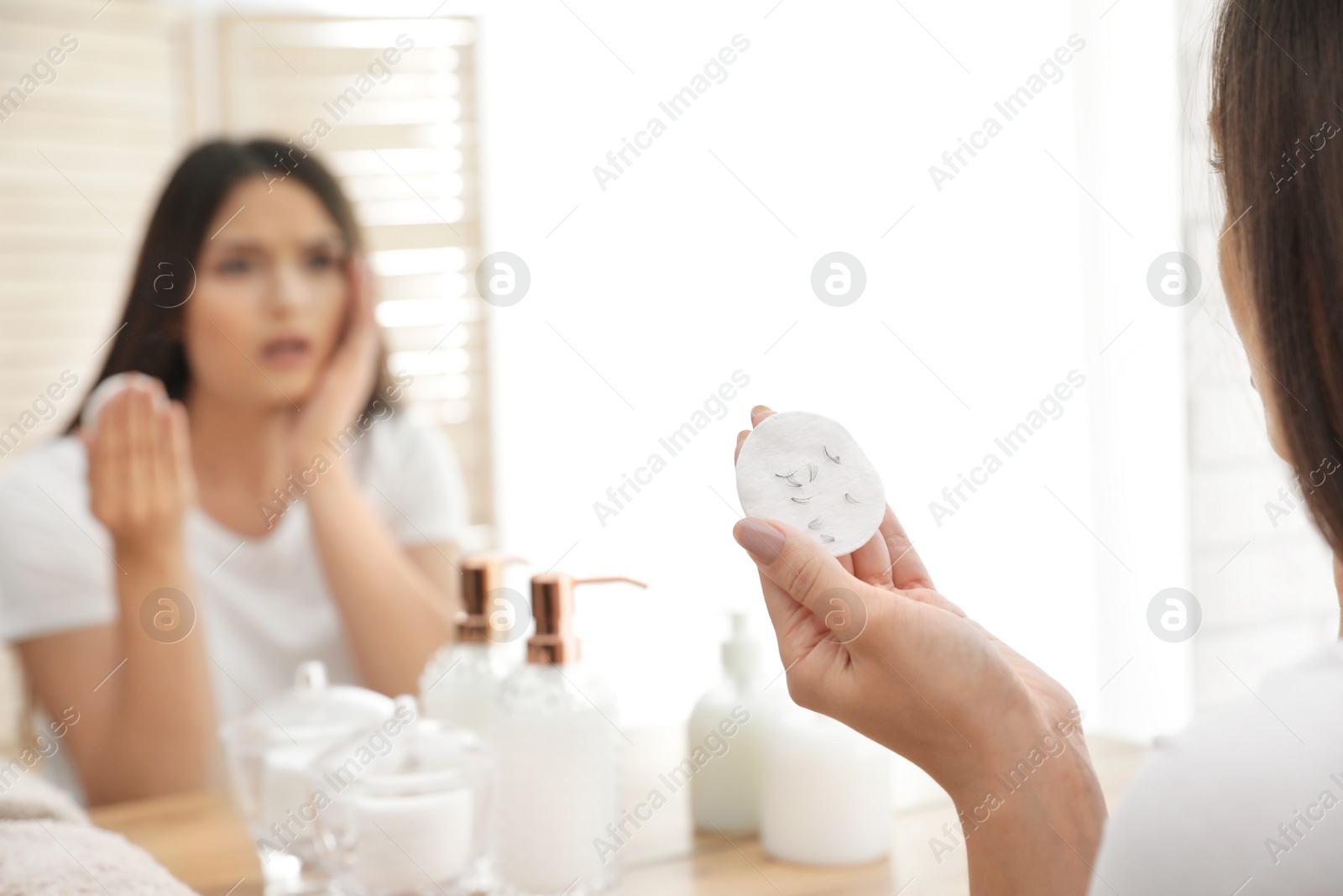 Photo of Beautiful woman holding cotton pad with fallen eyelashes near mirror indoors, closeup
