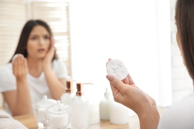 Photo of Beautiful woman holding cotton pad with fallen eyelashes near mirror indoors, closeup