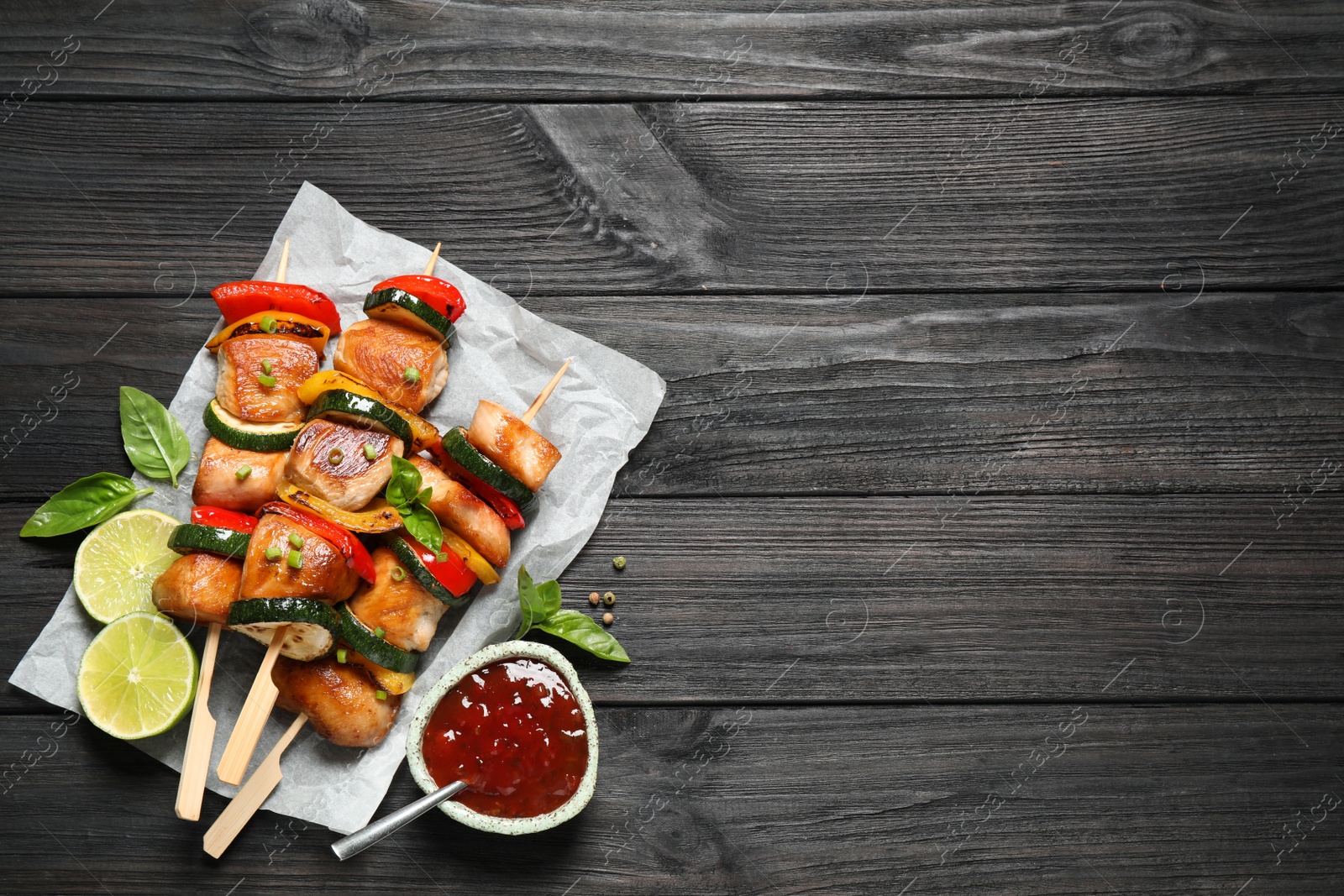 Photo of Delicious chicken shish kebabs with vegetables and ketchup on black wooden table, flat lay. Space for text