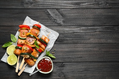 Photo of Delicious chicken shish kebabs with vegetables and ketchup on black wooden table, flat lay. Space for text