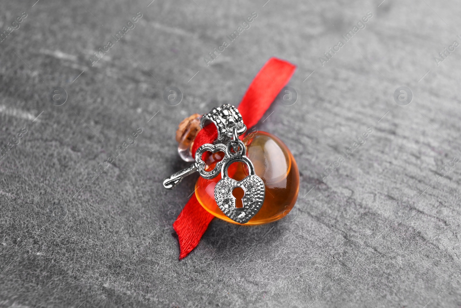 Photo of Heart shaped bottle of love potion with small key and padlock on grey table