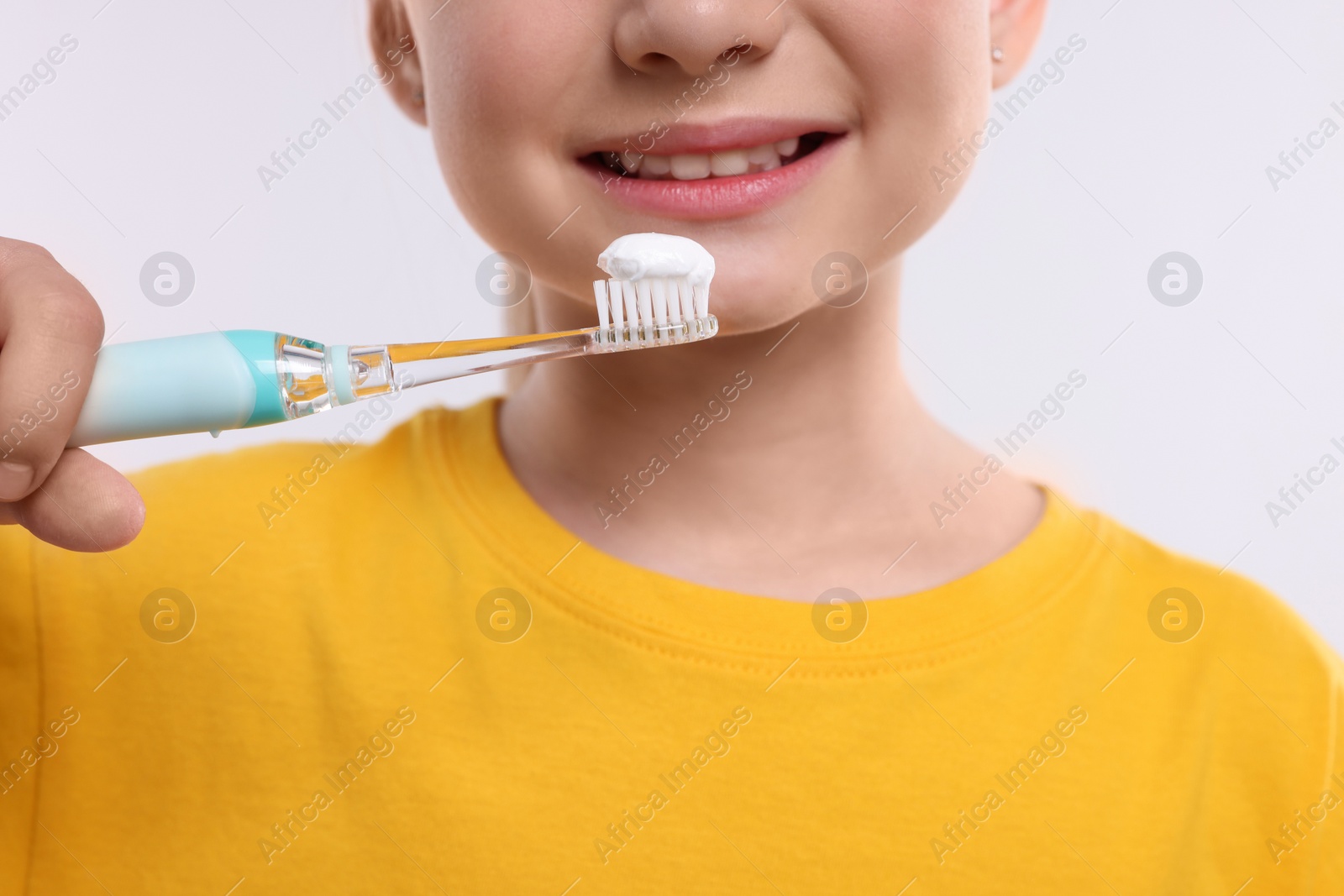 Photo of Happy girl brushing her teeth with electric toothbrush on white background, closeup