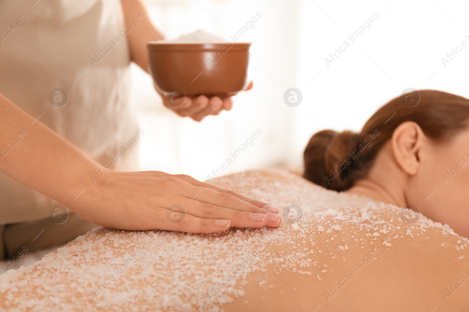 Photo of Young woman having body scrubbing procedure with sea salt in spa salon, closeup