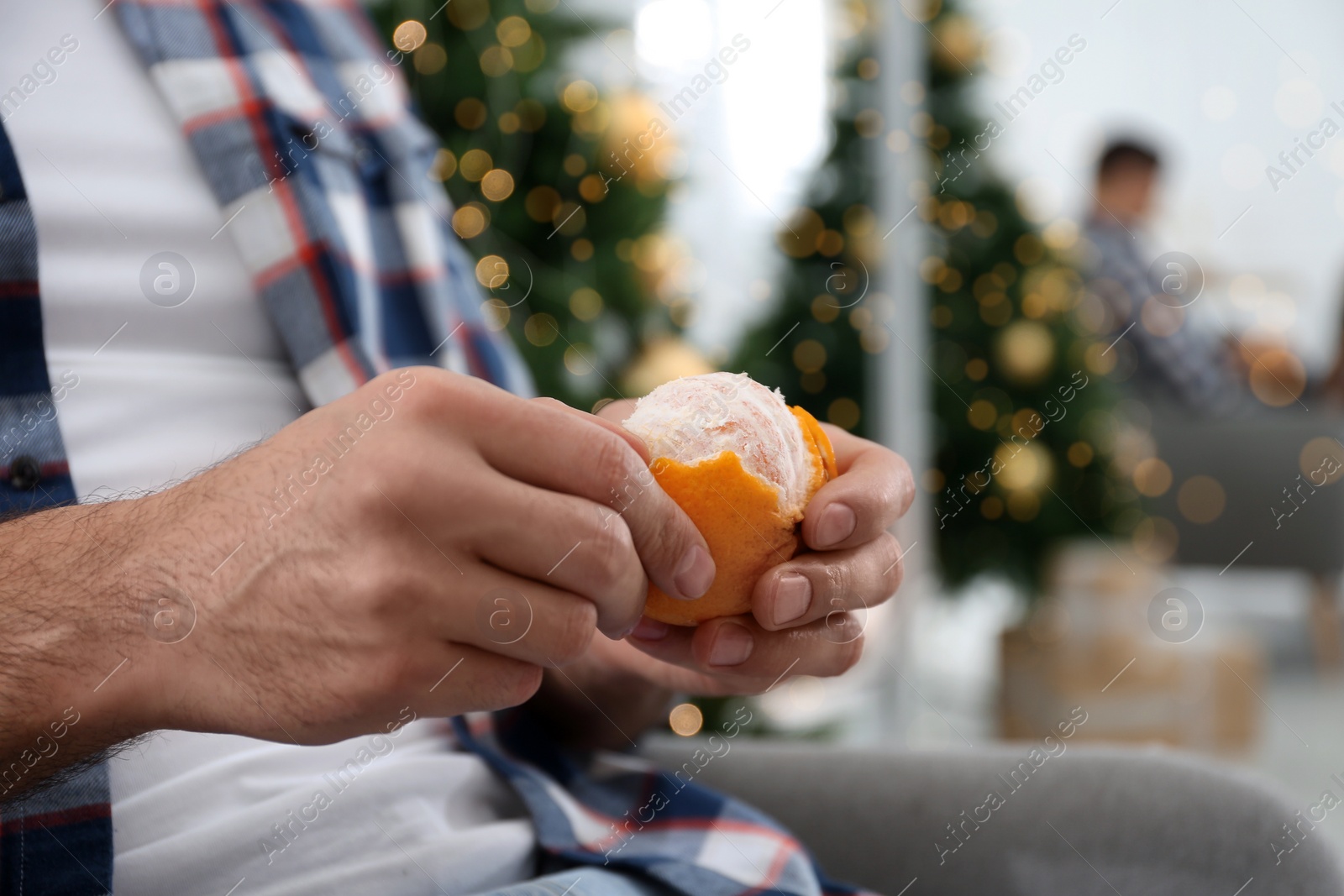 Photo of Man with tangerine near Christmas tree, closeup