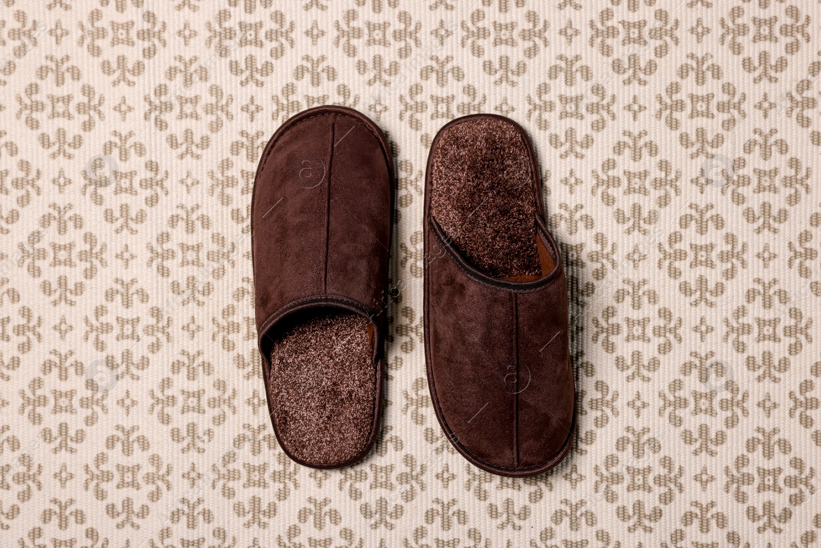 Photo of Brown slippers on patterned carpet, top view