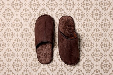 Photo of Brown slippers on patterned carpet, top view