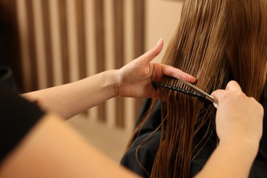 Professional hairdresser combing girl's hair in beauty salon, closeup