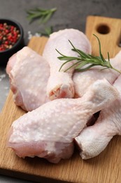 Photo of Raw chicken drumsticks with rosemary on wooden board, closeup