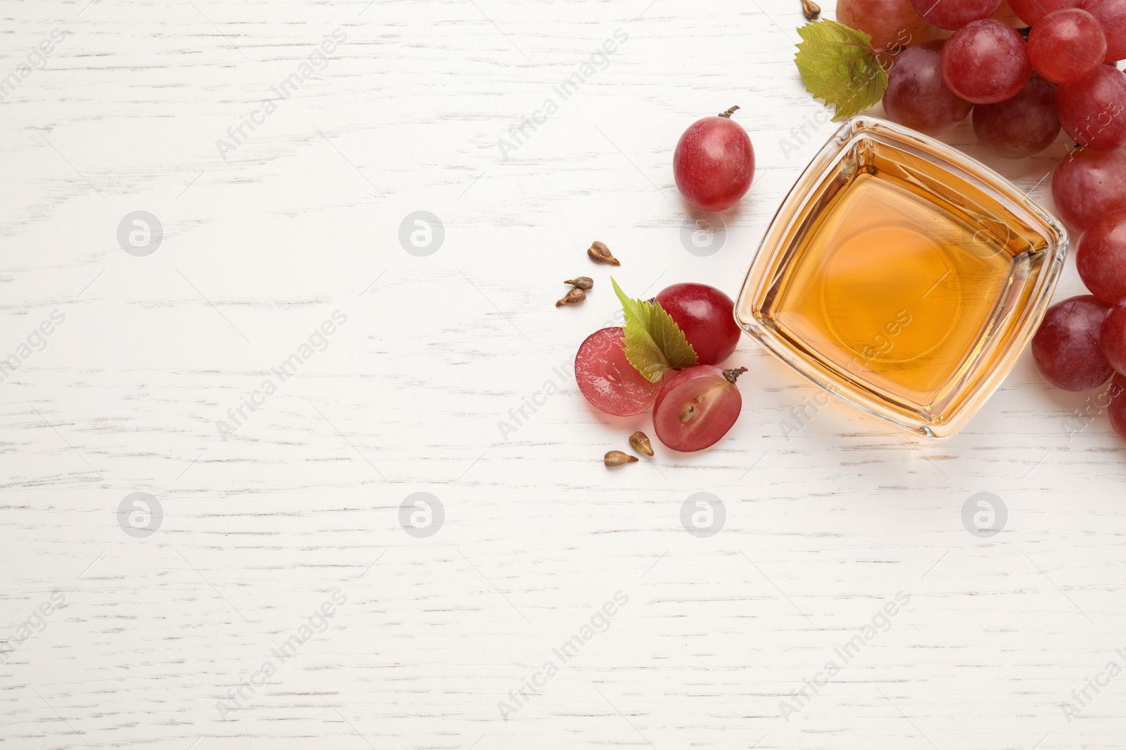 Photo of Flat lay composition with bowl of natural grape seed oil on white wooden table, space for text. Organic cosmetic