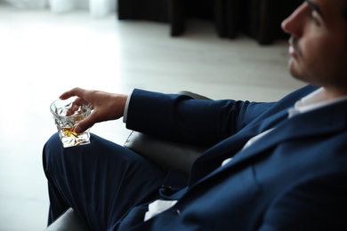 Photo of Young man with glass of whiskey indoors, closeup