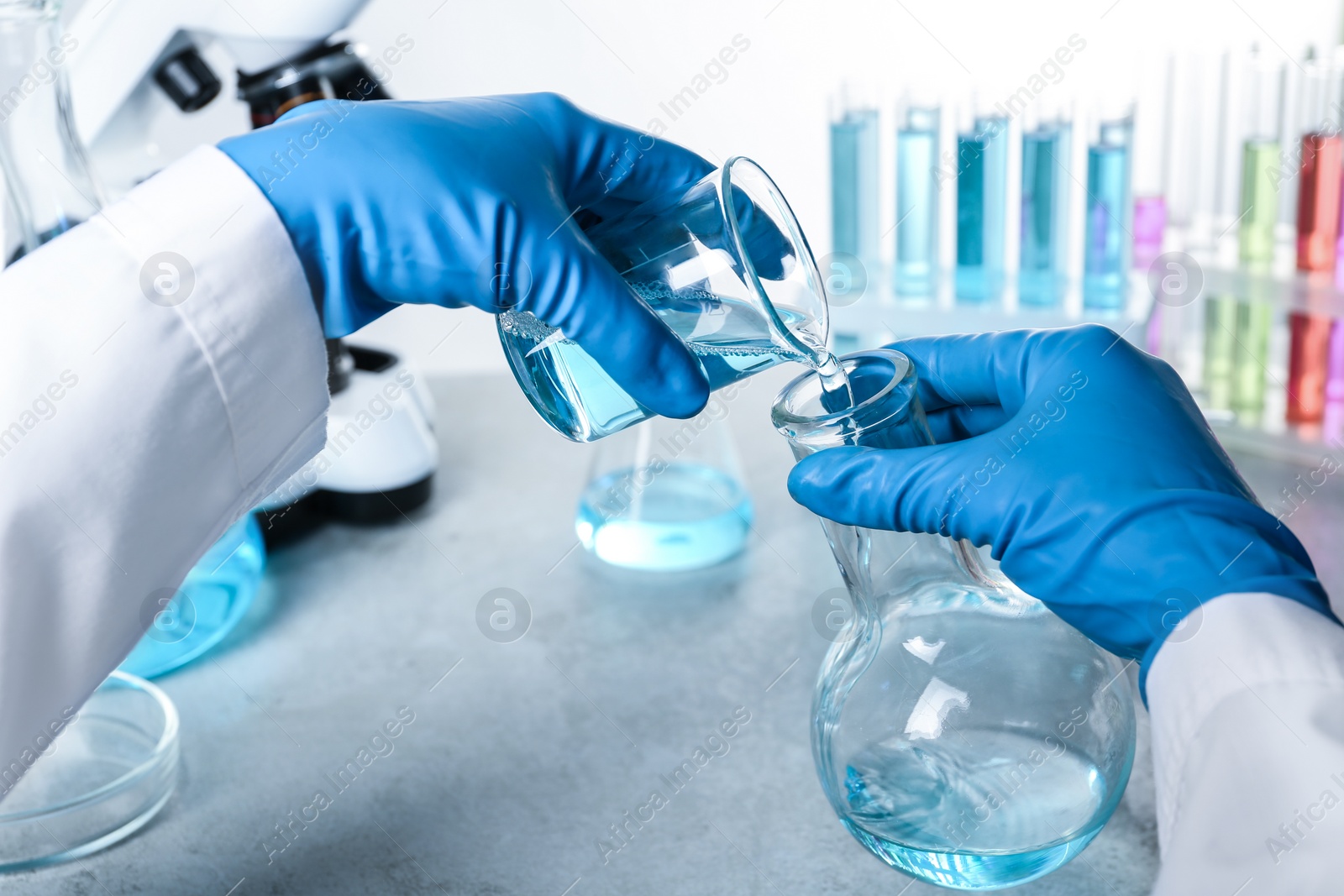 Photo of Scientist pouring color liquid from beaker into Florence flask over table, closeup. Solution chemistry