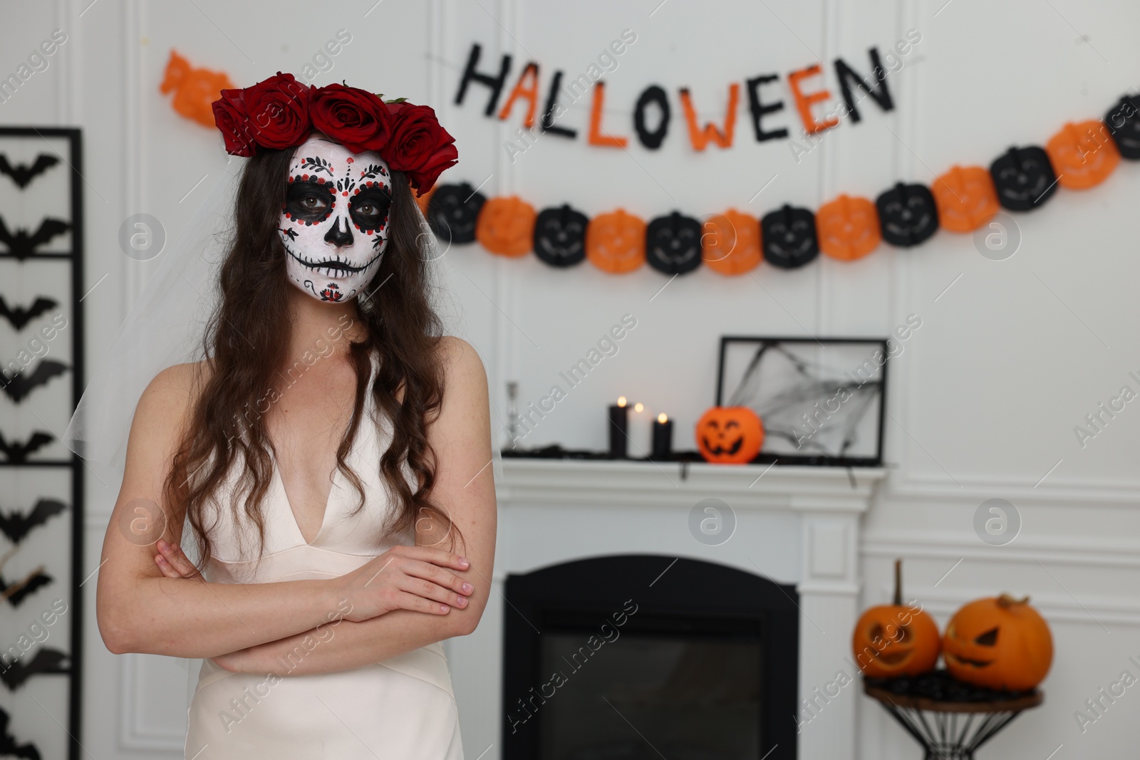 Photo of Young woman in scary bride costume with sugar skull makeup and flower crown indoors, space for text. Halloween celebration