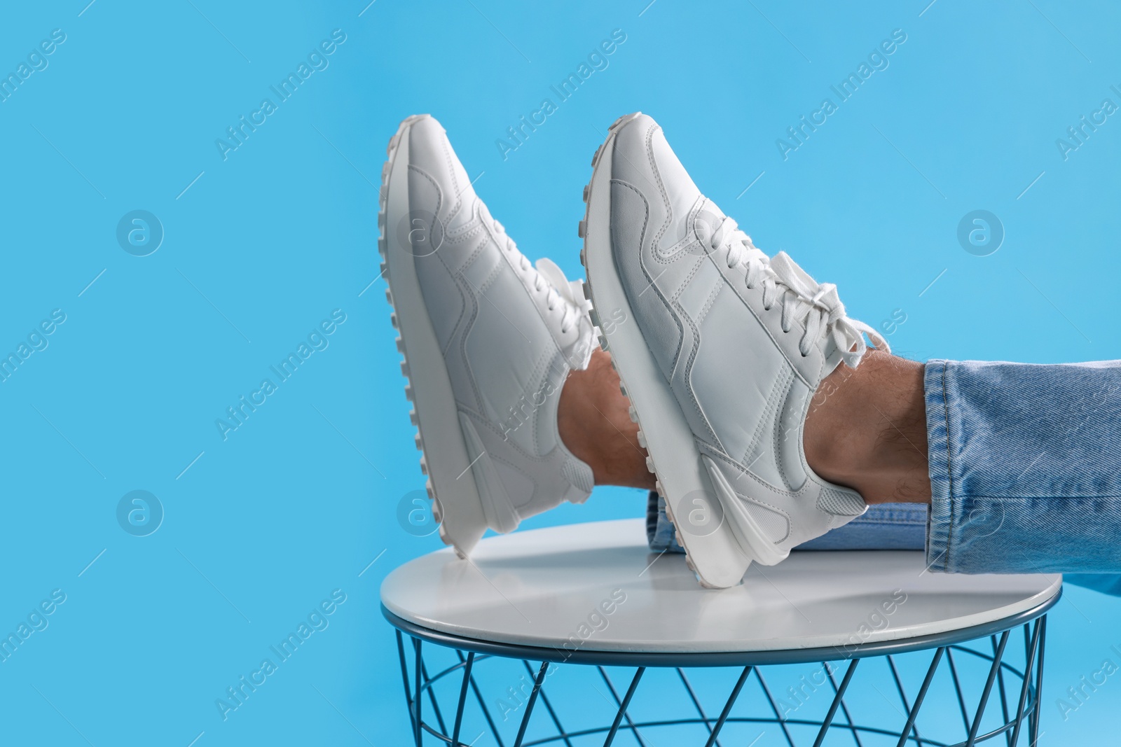 Photo of Man wearing stylish sneakers on white table against light blue background, closeup