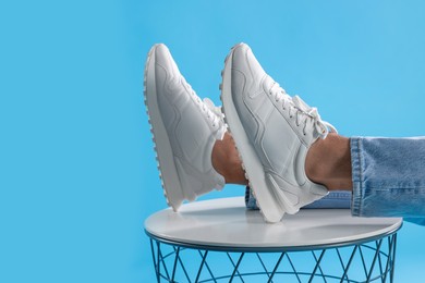 Man wearing stylish sneakers on white table against light blue background, closeup