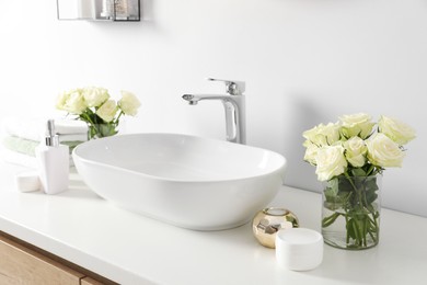 Photo of White sink between beautiful roses and toiletries in bathroom