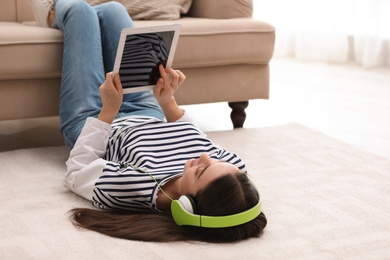 Photo of Young woman with headphones and tablet listening to music on floor in living room