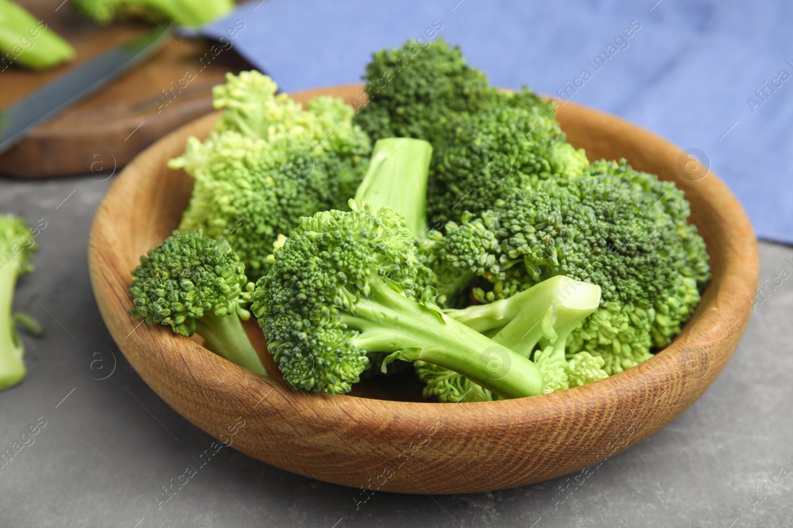 Photo of Fresh green broccoli in wooden bowl on grey table, closeup