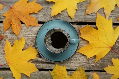 Cup of hot coffee and autumn leaves on wooden table, flat lay