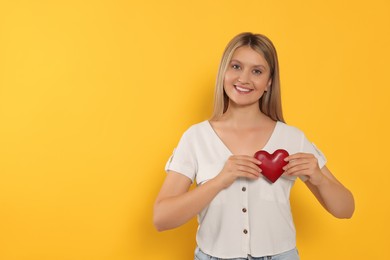 Happy volunteer holding red heart with hands on orange background. Space for text