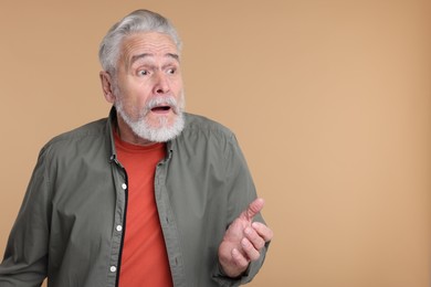 Portrait of surprised senior man on beige background, space for text