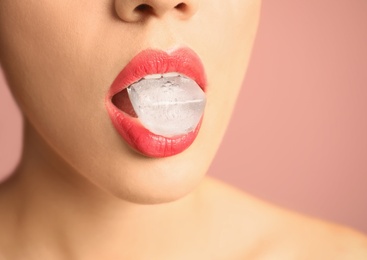 Photo of Young woman holding ice cube in mouth on color background, closeup